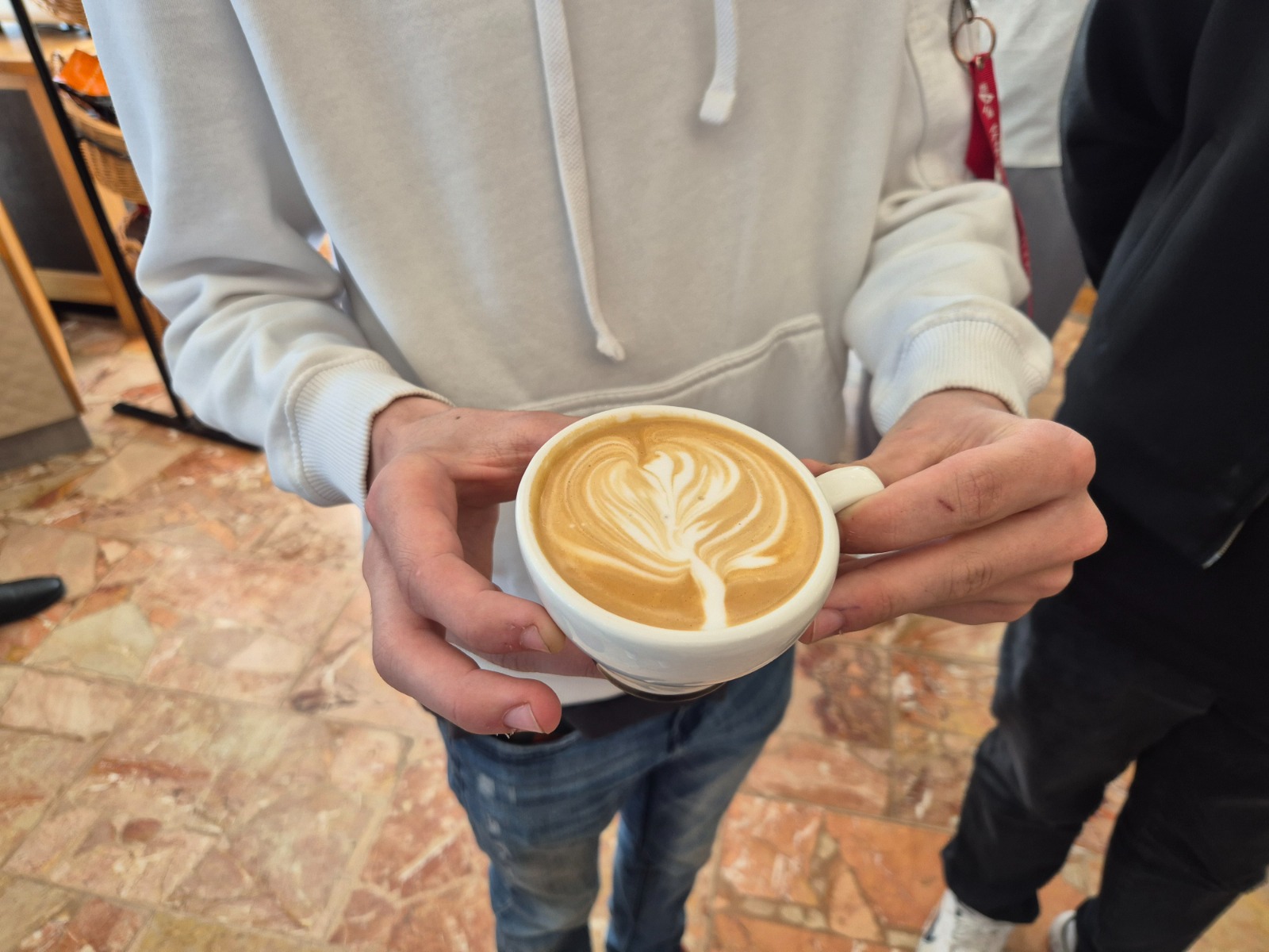Exkursion_Schärf 9 Ein:e Schüler:in hält eine Tasse Cappuccino mit kunstvoller Latte-Art in den Händen.