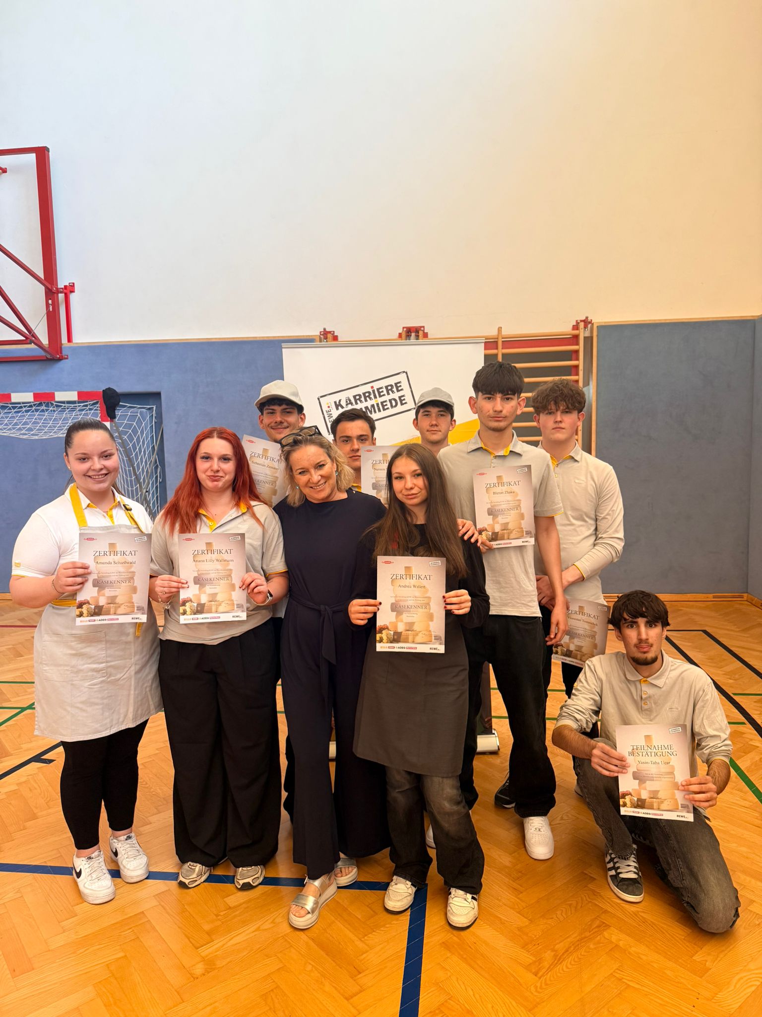 Käsekenner_4.LG_7 Gruppenfoto von Schüler*innen mit Zertifikaten in einer Turnhalle bei der Auszeichnungsfeier des Käsekenners.