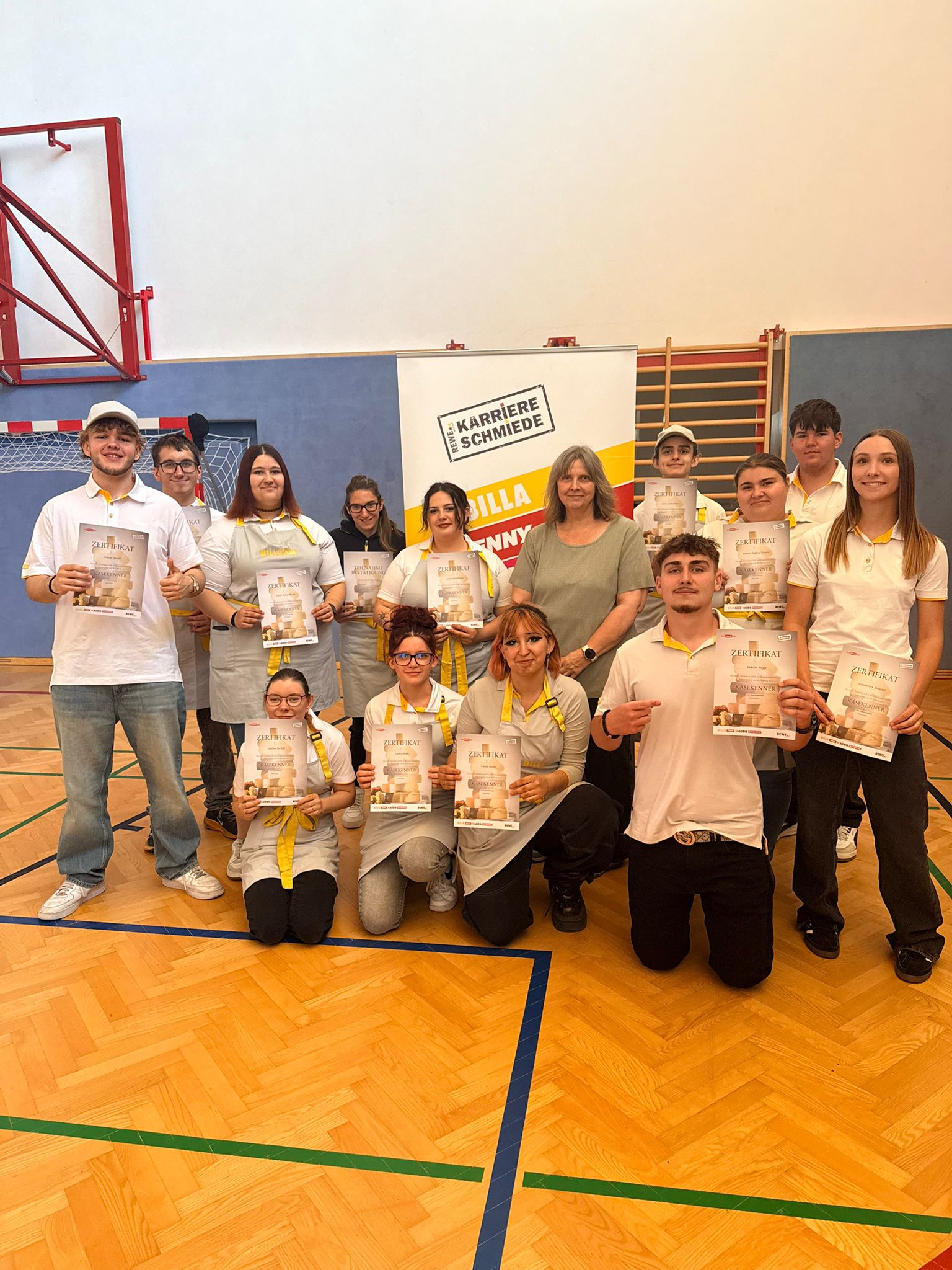 Käsekenner_4.LG_6 Gruppenfoto von Schüler*innen mit Zertifikaten in einer Turnhalle bei der Auszeichnungsfeier des Käsekenners.