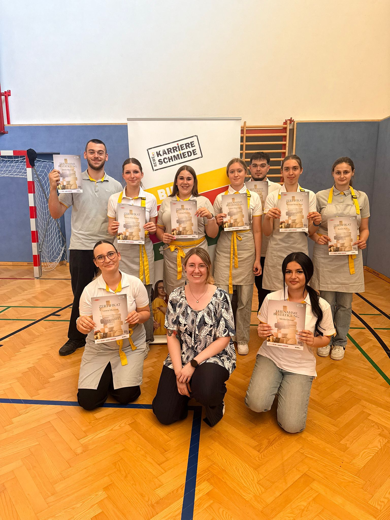 Käsekenner_4.LG_5 Gruppenfoto von Schüler*innen mit Zertifikaten in einer Turnhalle bei der Auszeichnungsfeier des Käsekenners.