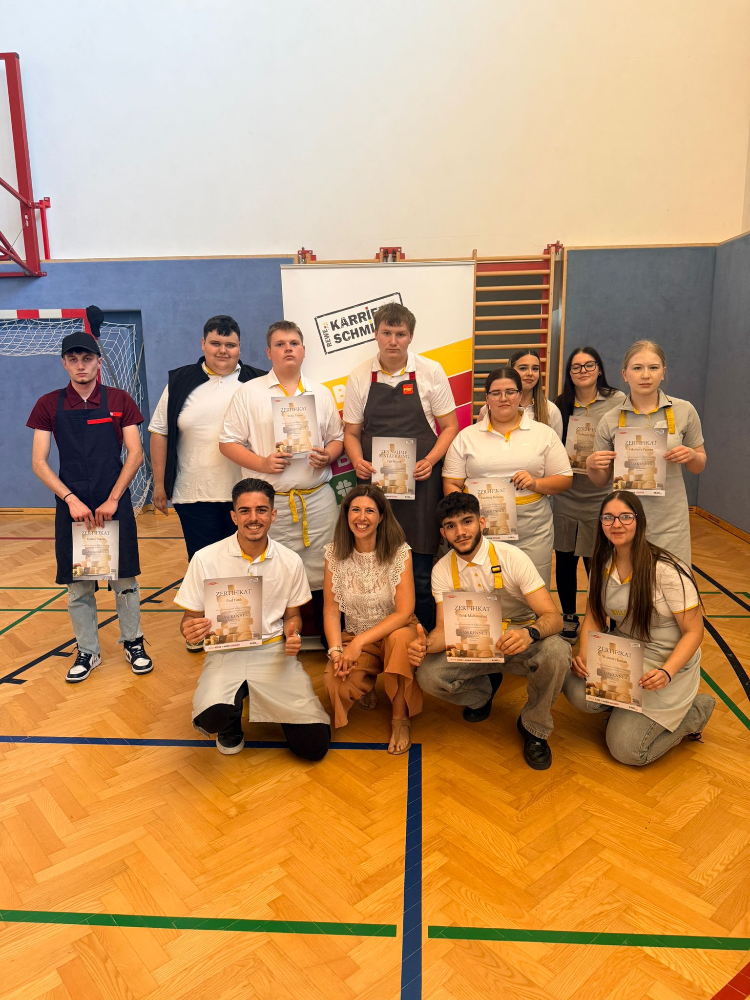 Käsekenner_4.LG_4 Gruppenfoto von Schüler*innen mit Zertifikaten in einer Turnhalle bei der Auszeichnungsfeier des Käsekenners.