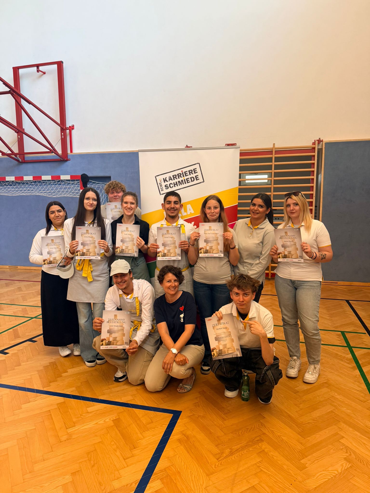 Käsekenner_4.LG_3 Gruppenfoto von Schüler*innen mit Zertifikaten in einer Turnhalle bei der Auszeichnungsfeier des Käsekenners.