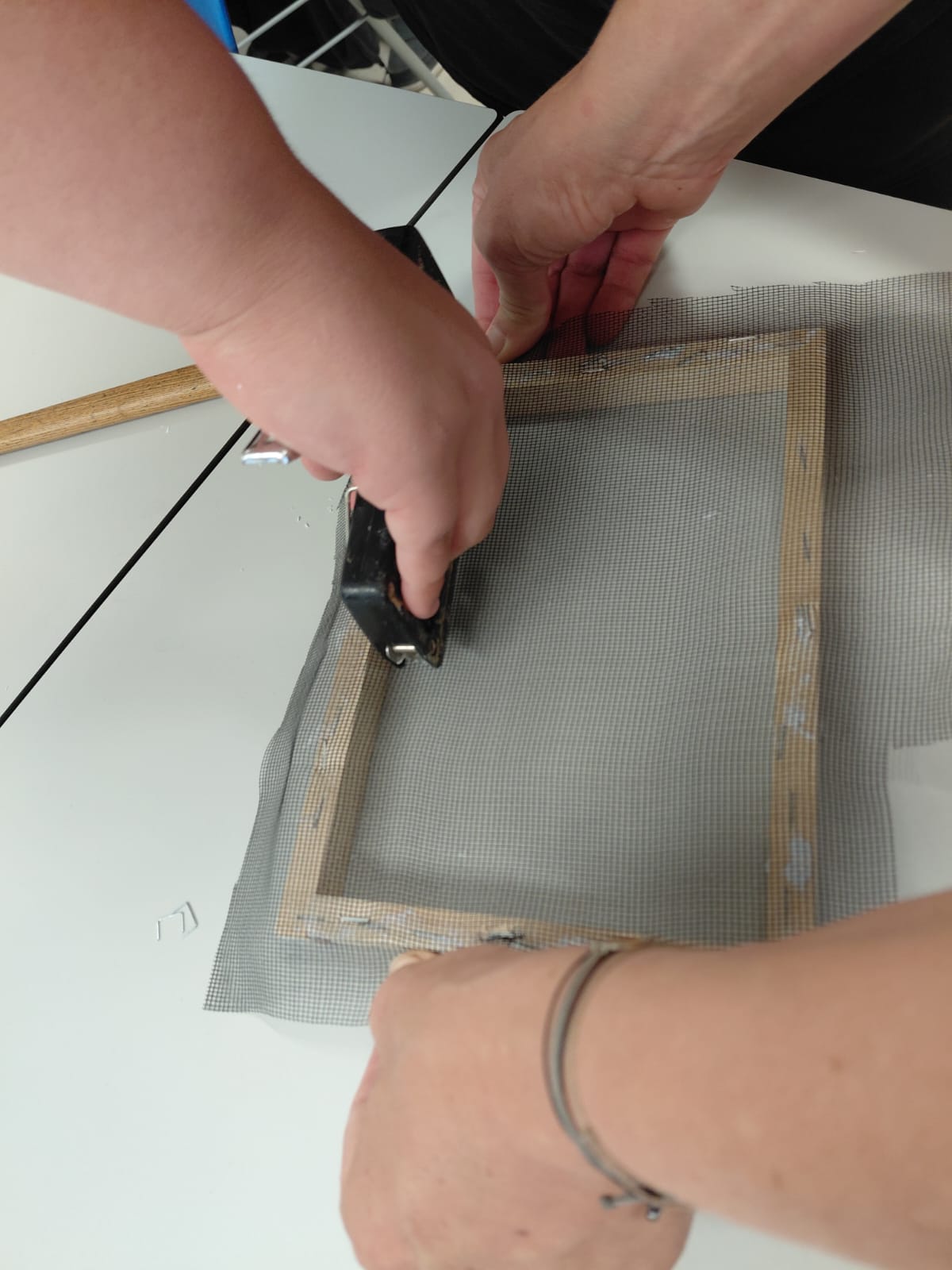 Workshop "Papierschöpfen" Zwei Hände halten einen Holzrahmen mit Netzbespannung fest, während eine dritte Hand diese festtackert.