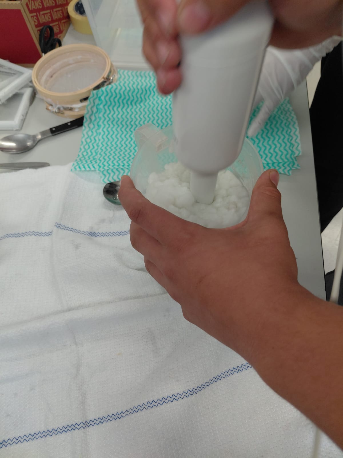 Workshop "Papierschöpfen" Eine Hand hält einen Plastikkrug, die andere einen weißen Stabmixer, der Papierbrei mixt.