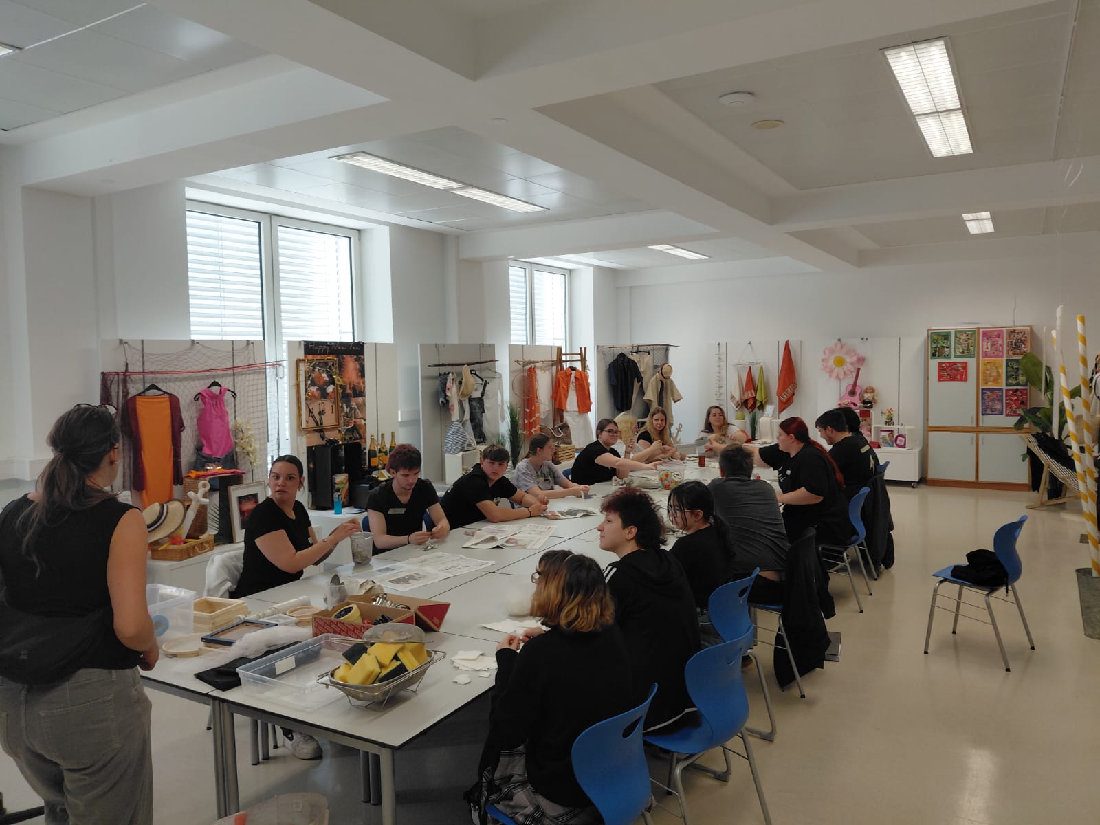 die 1. PA beim Workshop "Papierschöpfen" Größere Gruppe von Personen sitzt an mehreren zusammengestellten Tischen in einem hellen Raum und arbeitet gemeinsam.