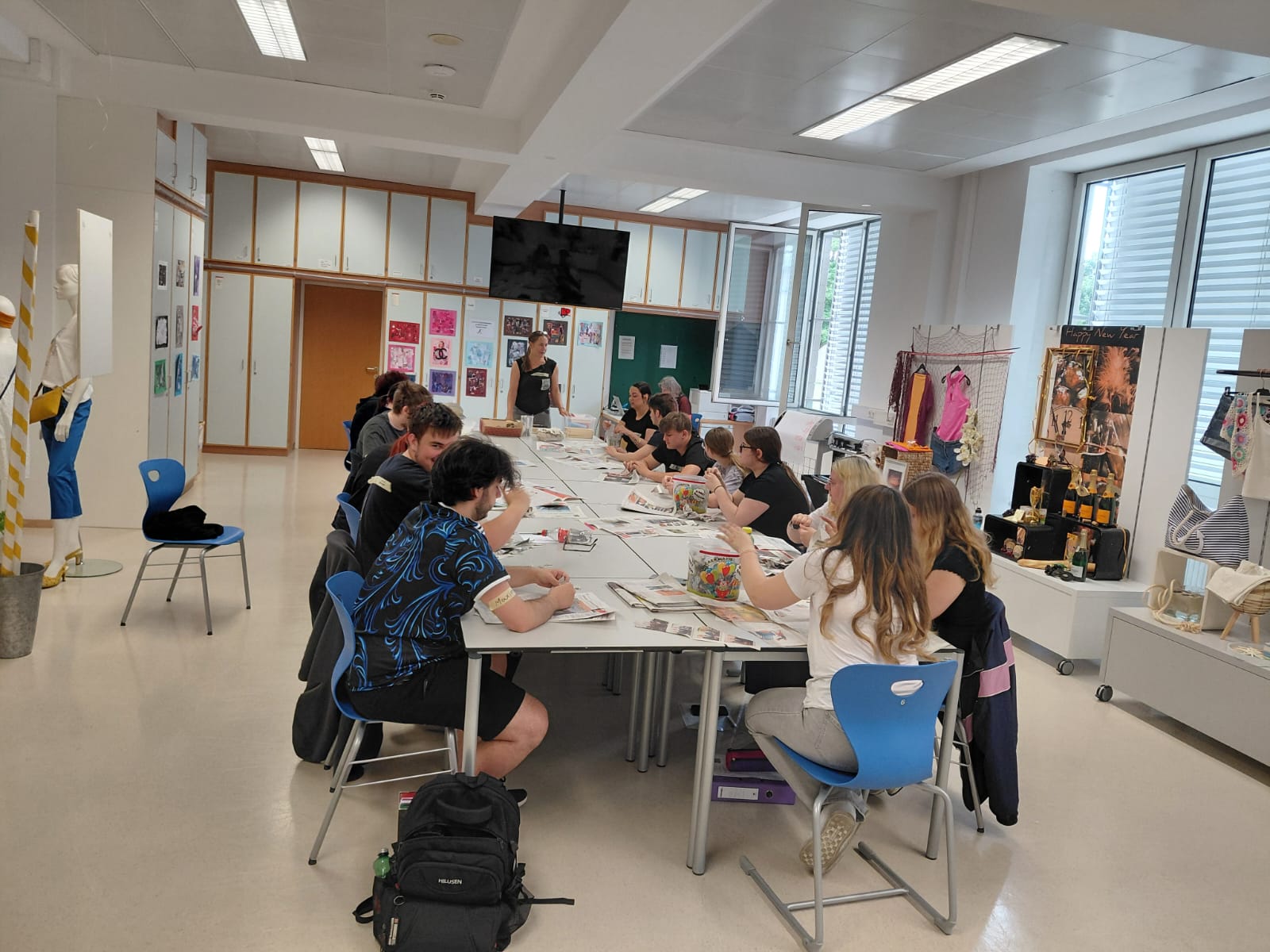 die 1. PA beim Workshop "Papierschöpfen" Größere Gruppe von Personen sitzt an mehreren zusammengestellten Tischen in einem hellen Raum und arbeitet gemeinsam.