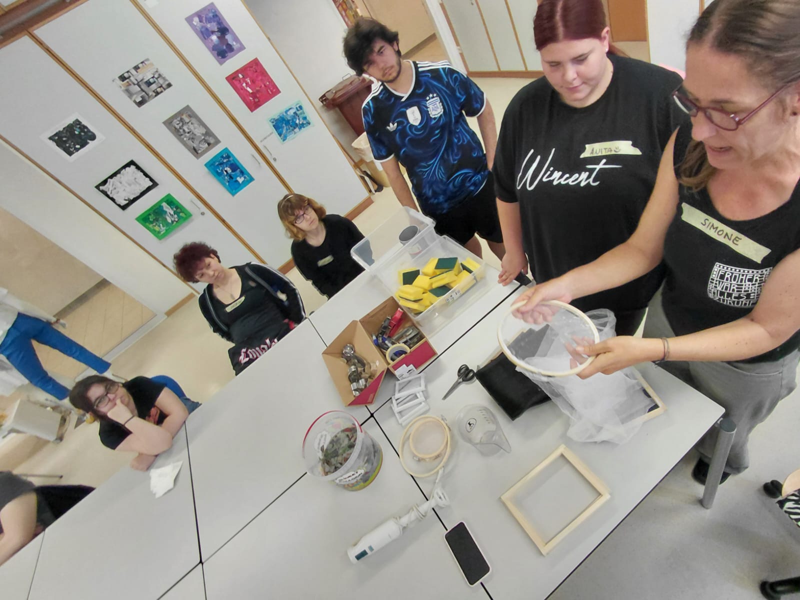 Schüler:innen der 1.PA beim Workshop "Papierschöpfen" Personen stehen an einem Arbeitstisch und arbeiten gemeinsam mit Werkzeugen und Materialien.