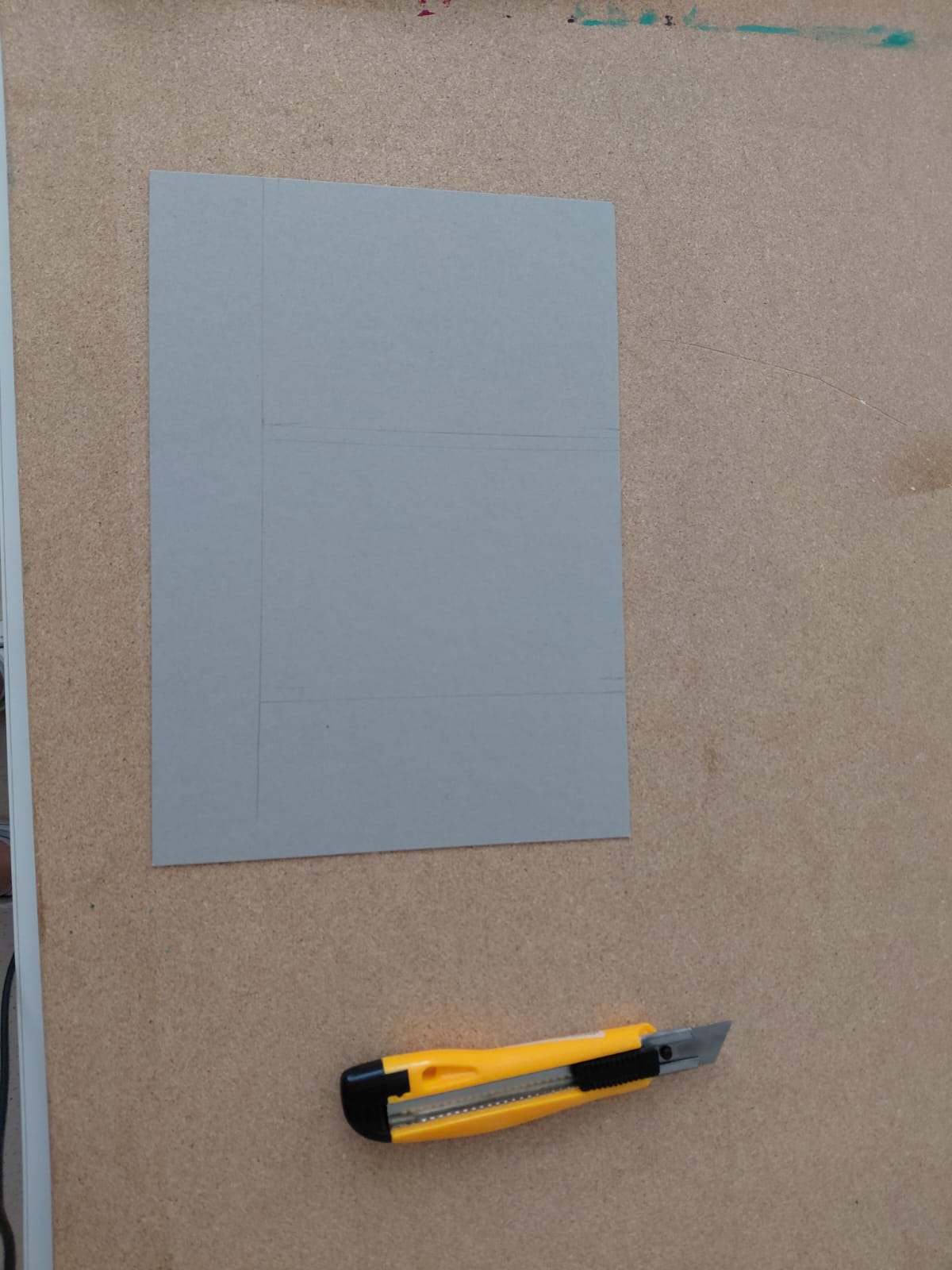 Workshop "Buchbinden" Ein Blatt graues Papier mit Bleistiftmarkierungen und ein Stanleymesser auf einer Spanplatte.