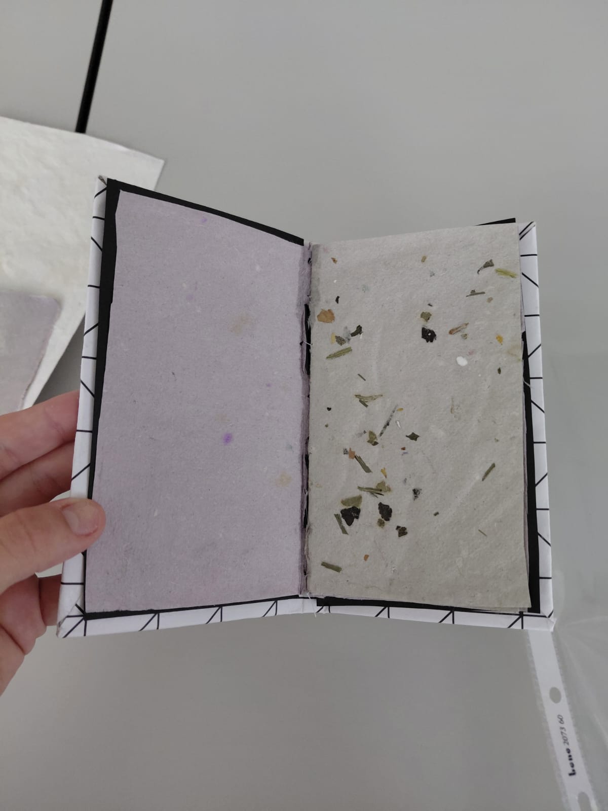 Workshop "Buchbinden" Eine Hand hält ein kleines Buch aus Büttenpapier und Blütenpapier.