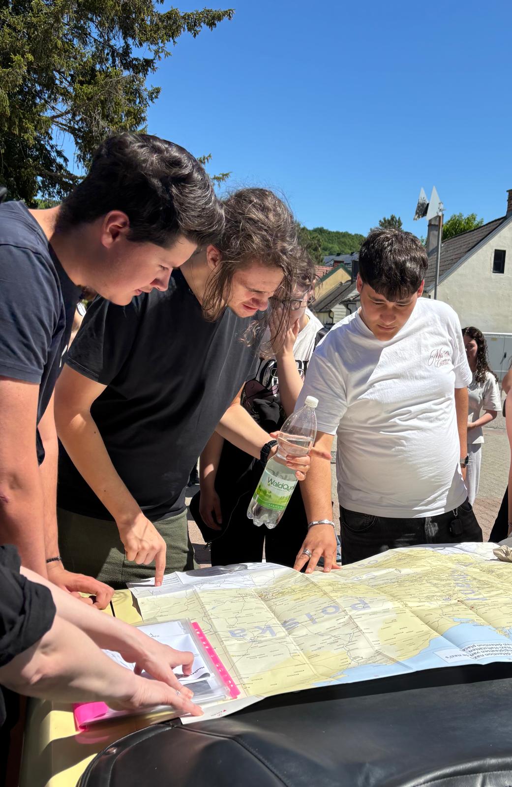 Lehrausgang_Hirtenberg_3 Drei Schüler:innen beugen sich über eine große Karte und besprechen gemeinsam den Weg im Freien.