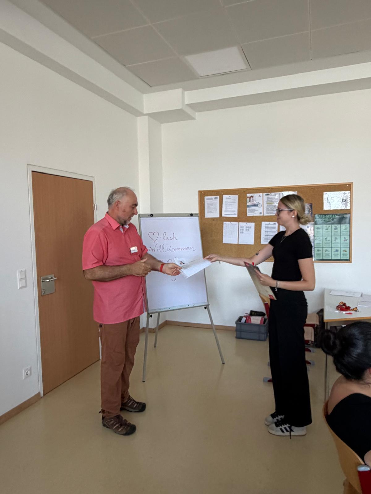 Workshop_AK_Bewerbung_6 Vortragende:r überreicht einer/m Schüler:in im Klassenzimmer Unterlagen im Rahmen eines Workshops.