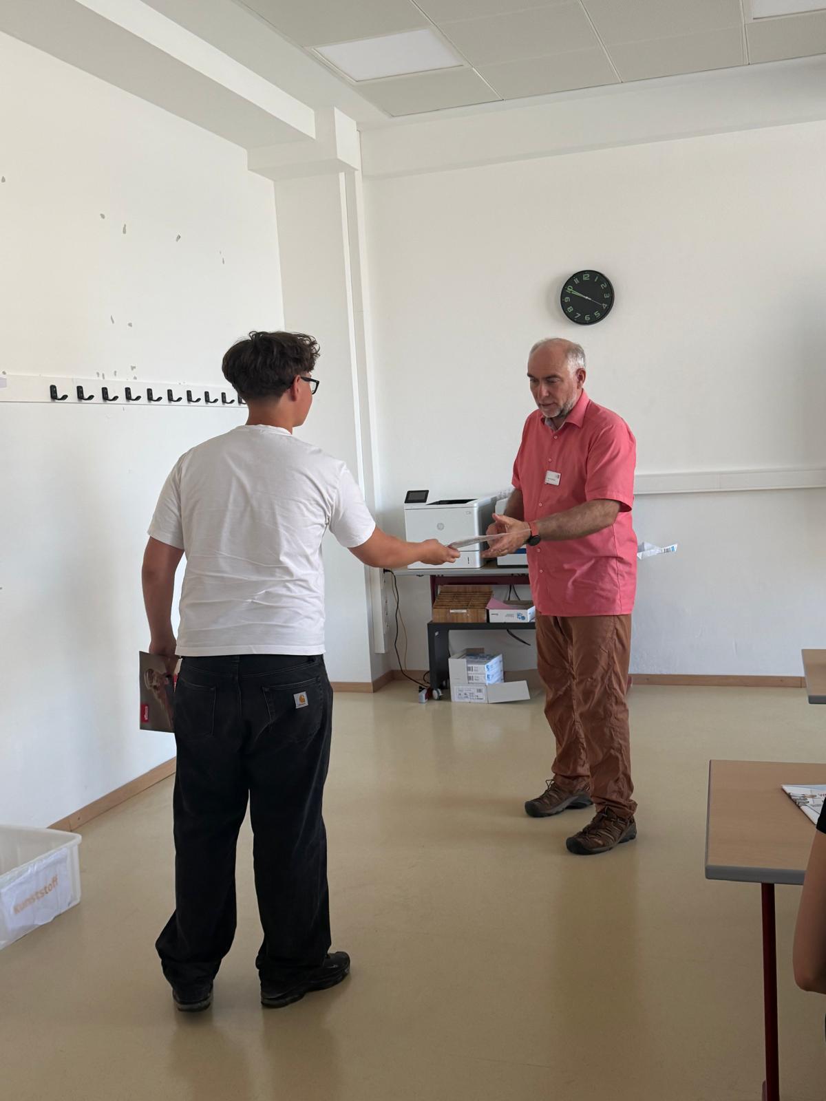 Workshop_AK_Bewerbung_5 In einem Klassenzimmer überreicht ein:e Schüler:in ein Blatt einer erwachsenen Person im Rahmen eines Workshops.