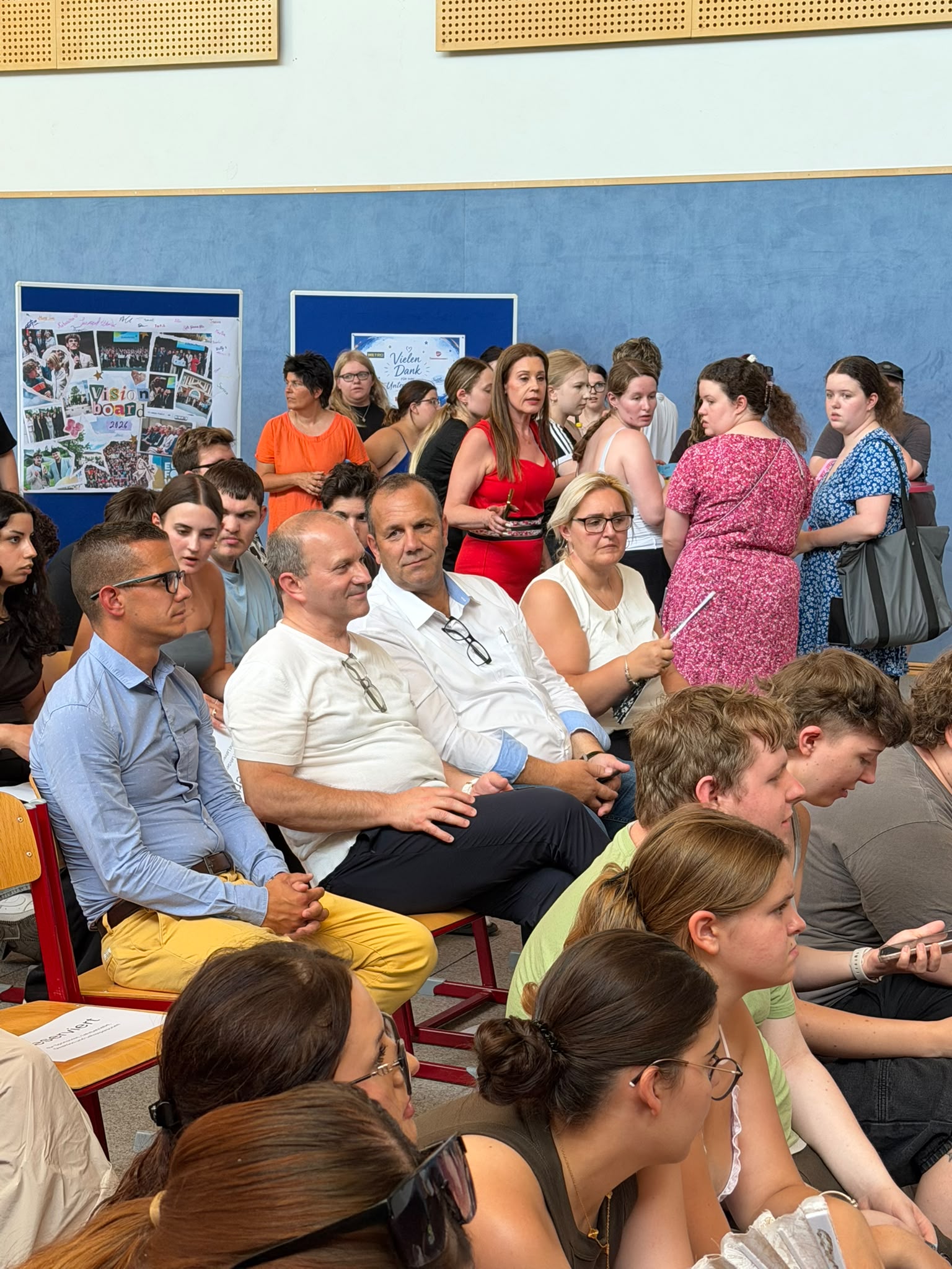 Abschlussfeier_The Road to Digital Freedom_4 Viele Teilnehmende sitzen und stehen bei einer schulischen Veranstaltung zum EU-Projekt "The Road to Digital Freedom" in der Turnhalle.