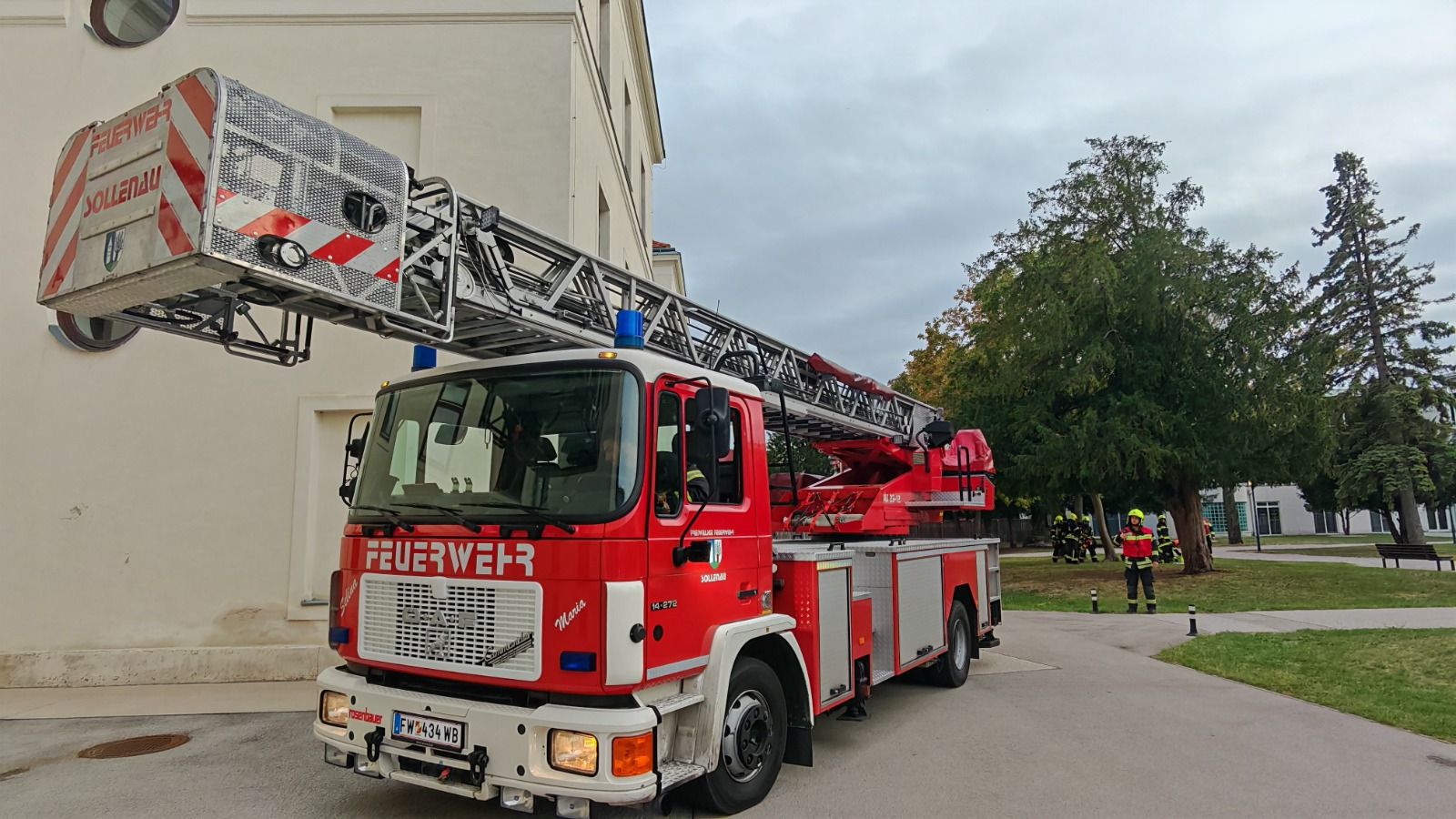 Feuerwehr Sollenau mit Drehleiter vor Gebäude, Männer in Einsatzkleidung im Hintergrund
