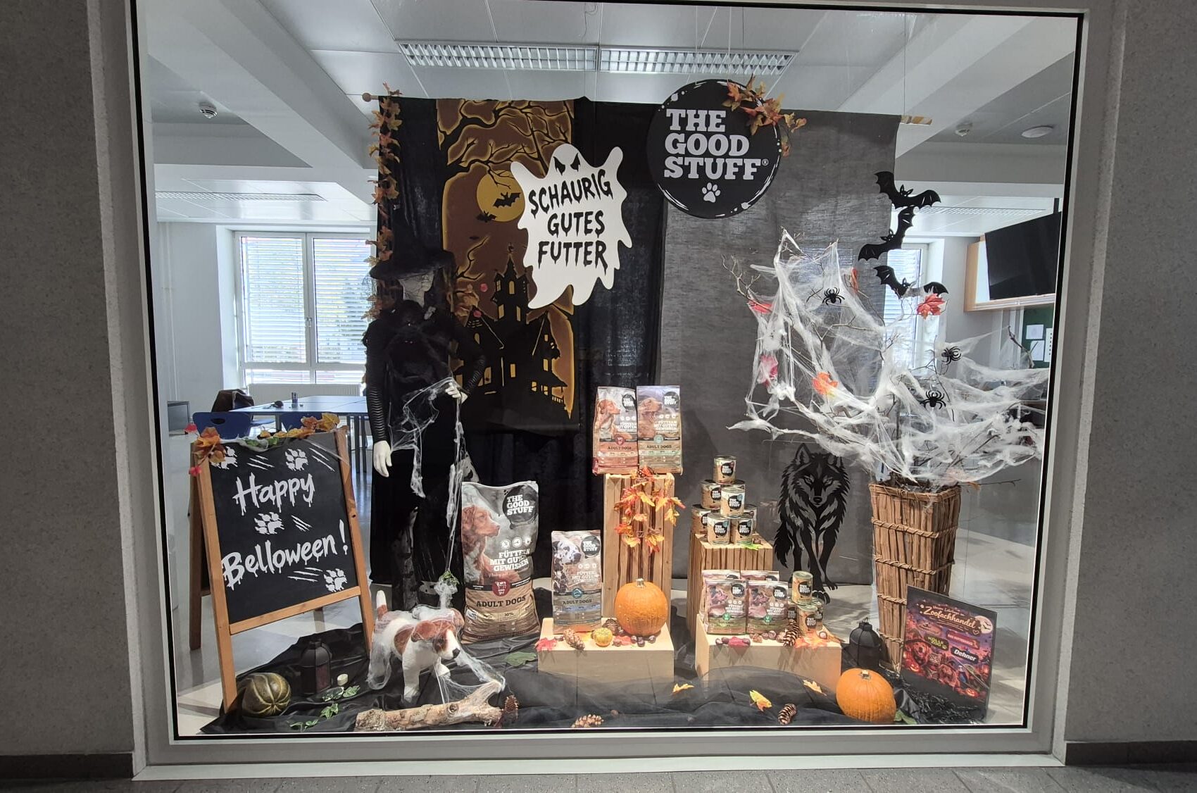 Halloween 2026 Halloween-Schaufenster mit Hunde- und Katzenfutter von THE GOODSTUFF, Kürbissen, Spinnweben, Fledermäusen und einer gruseligen Hexenfigur.
